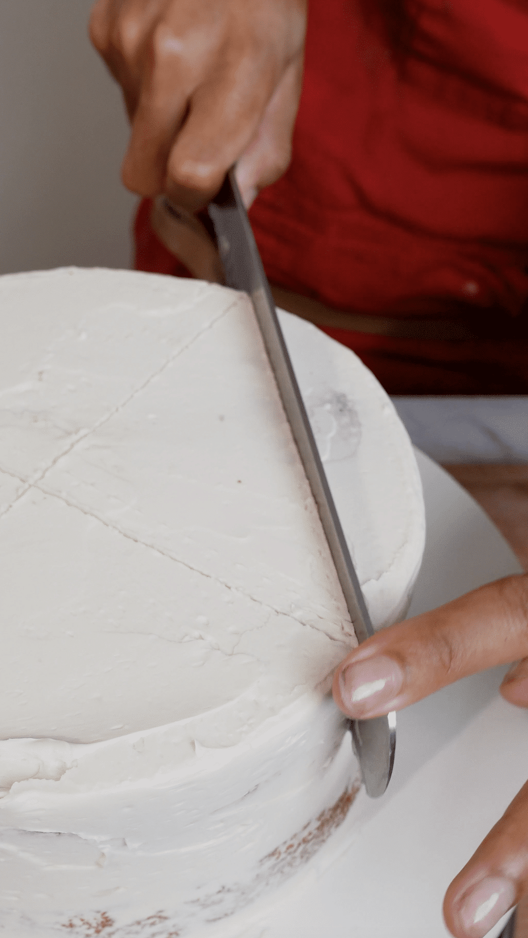Baker deepening the cross guide lines on top of a round cake to prepare for carving a heart shape.